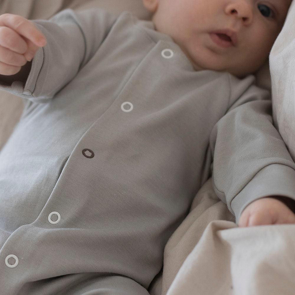 Newborn baby, wearing organic sleepsuit in light grey from The Sleepy Collection