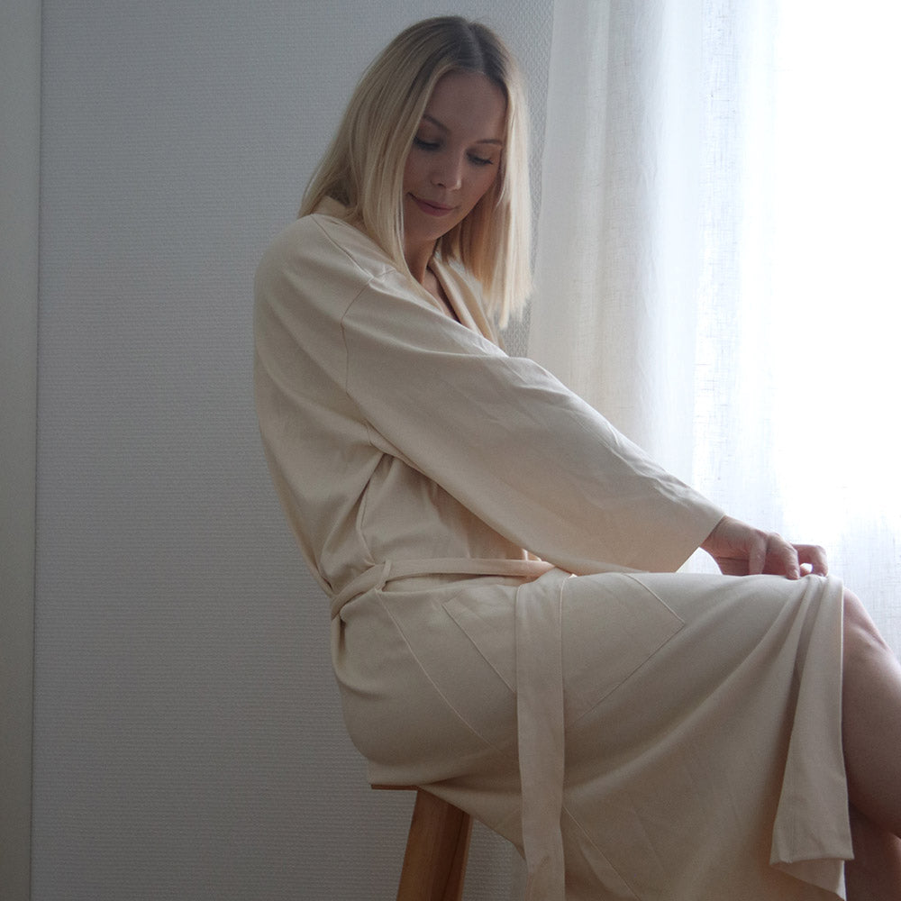 A woman wearing a luxurious morning robe in color sand from The Sleepy Collection