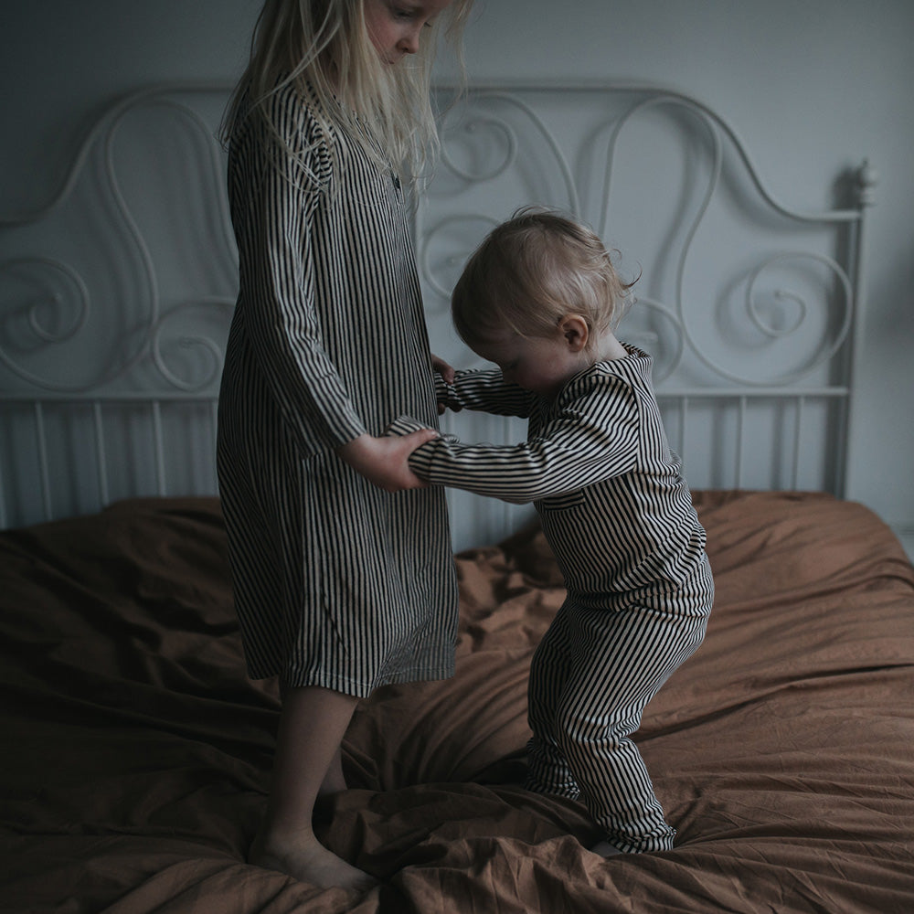 Siblings jumping in bed wearing sleepwear from The Sleepy Collection. Photo by Tiril Hauen